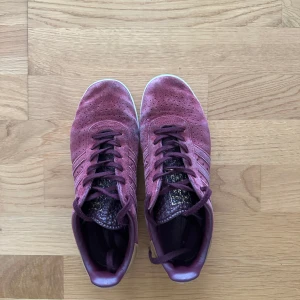 Vinröda Adidas 350 sneakers i mocka - Adidas 350 sneakers i vinröd mocka med gulddetaljer på häl och plös. Skorna har snörning, beige hälparti och vit sula. 