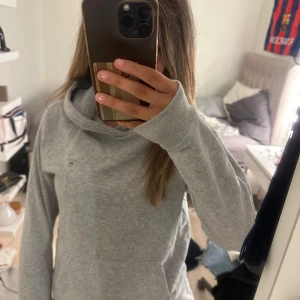 Grå hoodie från GANT - Säljer en grå hoodie från GANT med liten logga på bröstet. Tröjan har huva, lång ärm och en stor magficka framtill. Mjuk och skön bomullsmix, perfekt för chill dagar. Klassisk passform och stilren look som funkar till jeans eller mjukis. Original pris 750kr