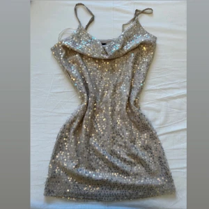Champagnefärgad glittrig paljettklänning - Säljer en kort, champagnefärgad klänning med tunna axelband och glittriga paljetter över hela tyget. Klänningen har en snygg draperad halsringning och är perfekt för dig som vill sticka ut med en festlig look. Materialet känns mjukt och följsamt mot kroppen. 💞