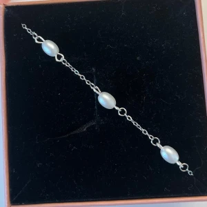 Silverarmband med vita pärlor - Stilrent armband i silverfärgad kedja med ovala vita pärlor jämnt fördelade runt hela armbandet. Kedjan är tunn och smidig, och pärlorna ger en elegant och klassisk känsla. Perfekt för dig som gillar en clean och tidlös look. I rostfritt stål och handgjort