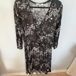 Blommig långklänning Odd Molly - Supersnygg långklänning från Odd Molly med blommigt mönster i svart, grått och beige. Klänningen har v-ringning, omlott-look och långa ärmar. Aldrig använd. Storlek 1 enligt oddmolly vilket motsvarar ungefär storlek S/36. Nypris ca 2000 kr. 