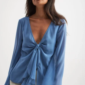 Blå omlottblus från NA-KD - Supersnygg blå omlottblus från NA-KD med en knytning framtill. Perfekt att styla med jeans eller kjol för en trendig outfit. Storlek 36, otroligt smickrande men har ej kommit till användning🩵🥰