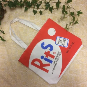 Retro shoppingväska med Rits-tryck - Cool shoppingväska med retroinspirerat Rits-tryck i rött, blått och vitt. Väskan har rejäla vita handtag och är perfekt för att bära böcker eller mat. Den fyrkantiga formen och det färgglada trycket gör den till ett riktigt statement-piece.