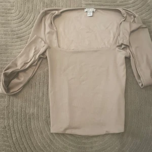 Beige långärmad topp från Amisu - Säljer en stilren beige långärmad topp från Amisu med fyrkantig urringning. Toppen har en slät och mjuk yta, figurnära passform och är perfekt att styla med jeans eller kjol. Enkel men trendig design som passar till många looks.