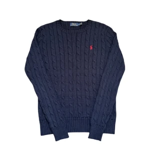 stickad Ralph Lauren - Säljer en klassisk mörkblå kabelstickad tröja från Polo Ralph Lauren med röd broderad logga på bröstet. Tröjan är ganska liten i storleken men i väldigt bra skick.