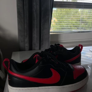 Nike sneakers svart/röd med snörning - Snygga Nike sneakers i svart och rött med klassisk röd swoosh på sidorna. Skorna har svart snörning,  Perfekta för dig som gillar streetwear och sportig look. Använda 3 gånger, nypris 750kr