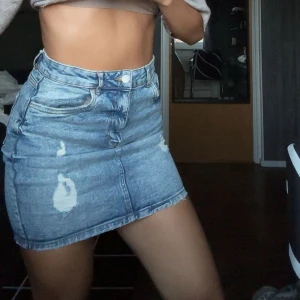 Blå jeanskjol med slitningar - Säljer en snygg blå jeanskjol med slitna detaljer och klassiska fickor både fram och bak endast använda 2 gånger💕