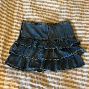 Volangkjol i jeans från Kappahl - Storleken är 140 men den sitter som en 146/152!💕Supersöt kort jeanskjol från Kappahl med flera volanger. Kjolen är blå och har en klassisk denimlook som ger en cool vibe. Perfekt för dig som gillar en lekfull och trendig stil. Passar till sneakers eller boots för en chill outfit.