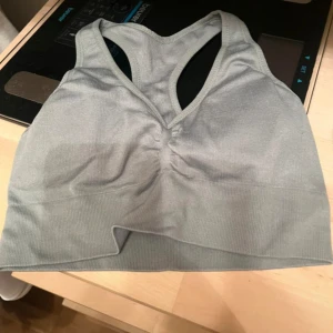 Grå sporttopp - Säljer en grå sporttopp i syntetmaterial. Toppen har en racerback-design och är ribbad för extra komfort. Perfekt för träning och ger bra stöd.