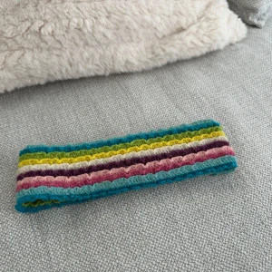 Flerfärgat stickat headband - Säljer ett färgglatt stickat hårband med ränder i turkos, rosa, lila, gul och beige. Perfekt för att liva upp vilken outfit som helst!