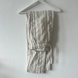 Randiga byxor från Zara - Snygga randiga byxor från Zara i beige och grått. Byxorna har en bekväm passform med elastisk midja och snörning. Perfekta för en avslappnad stil. Storlek L
