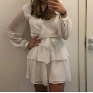 Vit omlottklänning med prickiga ärmar - Säljer min super söta klänning! Perfekt till studenten/ avslutningen eller bara till sommaren! Passar xs- m då den har ett band som man knyter i midjan. Endast använd 1 gång!