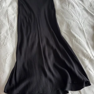 Svart långkjol från KappAhl - Elegant svart långkjol från KappAhl i en slät och mjuk design. Perfekt för en stilren look med sin långa längd och klassiska svarta färg.