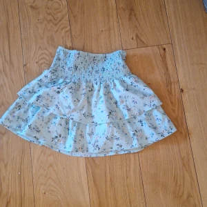 Kjol - Söt blommig kjol från Gina Tricot i ljusblått med volanger. Perfekt för en somrig look. Den har en elastisk midja för extra komfort. 🌸