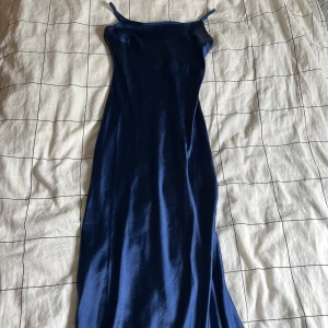 Marinblå långklänning från Gina Tricot - Snygg marinblå långklänning från Gina Tricot med smala axelband. Perfekt för en elegant look. Klänningen har en slät och glansig yta som ger en lyxig känsla. Perfekt till bal!