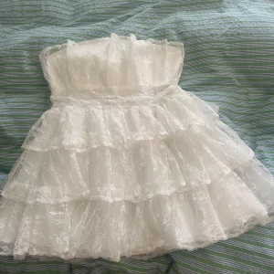 Vit spetsklänning med volanger  - Säljer en jättefin axelbandslös klänning köpt på Asos. Perfekt till studenten som jag köpte den till, den är endast testad då jag körde på en annan. Storleken är 44 och passar mig som har 42/44.💕