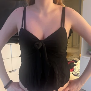 Svart linnetopp med knyt - Snygg svart linnetopp med smala axelband och knyt framtill. Perfekt för en stilren look.