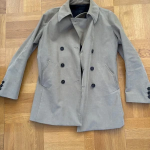 Pretty green rock från Liam Gallagher Collection  - Snygg beige kappa med dubbelknäppning och klassisk krage. Jackan har långa ärmar och två framfickor. Insidan är fodrad med ett mörkt tyg för extra komfort. Perfekt för höst och vår! Funkar i både L och M.
