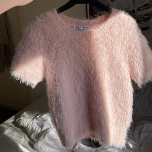 Rosa fluffig tröja från Zara - Säljer en supermjuk och fluffig rosa tröja från Zara. Den har korta ärmar och en rund halsringning, perfekt för en mysig look. Tröjan är gjord i ett syntetmaterial som ger en härlig textur. Passar perfekt för både vardag och speciella tillfällen. 🌸