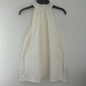 Halter neck top från Amisu  - Elegant vit ärmlös blus med hög krage och knytband i nacken. Perfekt för en stilren look.