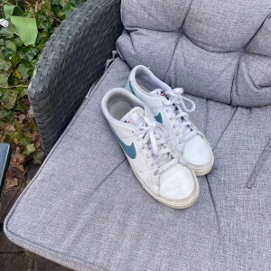 Vita Nike sneakers med blå detaljer - Säljer ett par vita Nike sneakers med blå swoosh och snörning. Perfekta för en avslappnad stil. Skorna har en klassisk design med rund tå och vit sula.