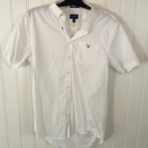 Vit kortärmad skjorta från Gant - Snygg vit kortärmad skjorta från Gant med klassisk krage och knappar framtill. Skjortan har en bröstficka med Gant-logga broderad. Perfekt för sommaren!