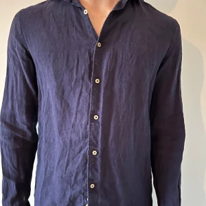 Mörkblå linneskjorta - Snygg mörkblå skjorta i linne med långa ärmar och knappar framtill. Perfekt för en stilren look.