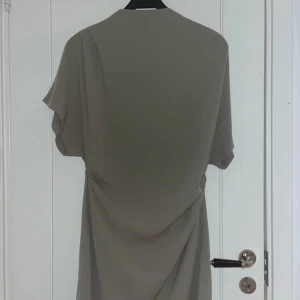 Grön/ beige  klänning med korta ärmar - Snygg grön/ beige klänning med korta ärmar och en elegant drapering på sidan. Perfekt för en stilren look.
