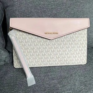 Kuvertväska från Michael Kors - Snygg kuvertväska från Michael Kors i en stilren design. Väskan har en ljusrosa läderflik och ett monogrammönster i beige och vitt. Perfekt för att bära det viktigaste med stil. Köpt i Usa