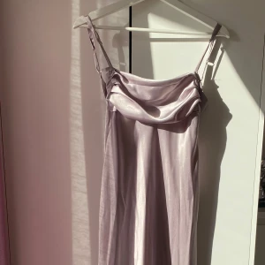 Ljuslila klänning från Zara - Säljer en elegant ljuslila klänning från Zara med smala axelband och en vacker drapering framtill. Klänningen har en öppen rygg och är tillverkad i ett glansigt material som ger en lyxig känsla. Perfekt för speciella tillfällen! (Satin lång klänning som slutar ungefär vid ankeln) Orginal pris: 499