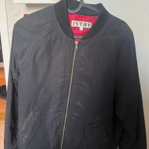 Svart bomberjacka från ISTAY - Säljer en stilren svart bomberjacka från ISTAY. Jackan har en dragkedja framtill och ribbade muddar vid krage, ärmslut och nederkant. Perfekt för en cool och avslappnad look.
