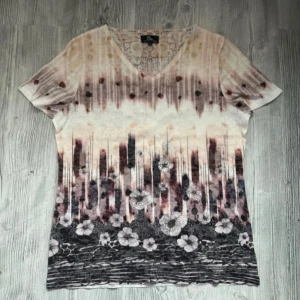 Mönstrad kortärmad topp från Alparadise Medium - Säljer en kortärmad topp från Alparadise med vackert blommönster och dekorativa detaljer. Toppen har en v-ringad spetsdetalj bak och ett färgskiftande mönster i jordnära toner. 