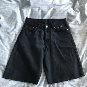 Sweet Sktbs Jorts - Säljer ett par svarta jeansshorts från Sweet Sktbs med fransiga kanter och klassisk femficksdesign. Perfekta för en avslappnad stil. De har en broderad logga på framsidan och är tillverkade i slitstarkt material.