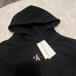 Svart hoodie från Calvin Klein Jeans - Snygg svart hoodie från Calvin Klein Jeans med klassisk logga på bröstet. Tröjan har en bekväm huva och långa ärmar med ribbade muddar. 