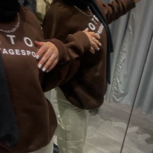 Brun sweatshirt med tryck - Säljer en brun sweatshirt med tryck på bröstet. Tröjan har långa ärmar och en avslappnad passform. Perfekt för en casual look.