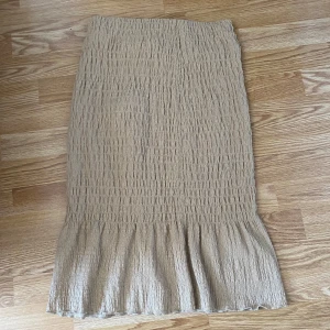 Beige kjol från Gina Tricot - Säljer en beige kjol från Gina Tricot med en volangdetalj vid fållen. Kjolen har en texturerad yta som ger en fin look. Perfekt för att skapa en stilren outfit.