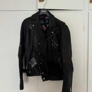 The Kooples x Orlinski Skinnjacka - Svart skinnjacka från The Kooples med graffiti-inspirerade tryck i olika färger. Limited Edt. Jackan har dragkedjor och knappar samt långa ärmar.