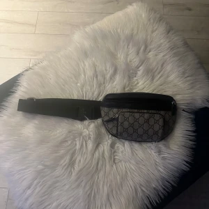 Mönstrad väska  - Snygg magväska med ett klassiskt mönster och dragkedja. Perfekt för att hålla dina saker säkra och nära till hands. Justerbart band för bekväm passform.