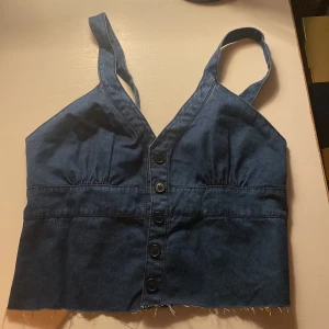 Blå jeanstopp - Säljer en blå jeanstopp som är avklippt från en klänning från h&m. den går att knäppa där fram och axelbanden går att justera.