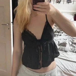 Svart linne från NA-KD - Säljer ett svart linne från NA-KD med spetsdetaljer och knytning framtill. Perfekt för en stilren look. Storlek 34.