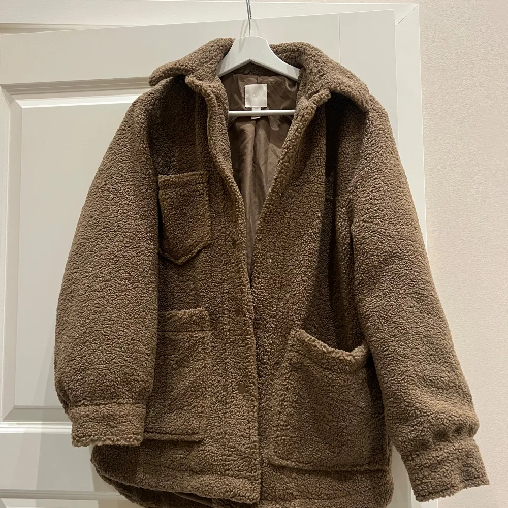 Helt oanvänd och jättemysig brun teddyjacka från H&M med långa ärmar och flera praktiska fickor. Perfekt för kyliga dagar när du vill hålla dig varm och bekväm. Jackan har en avslappnad passform och stängs med knappar framtill. ❤️. Takit.