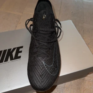 Svarta Nike fotbollsskor - Säljer ett par svarta Nike Mercurial Vapor 16 Elite AG-Pro fotbollsskor. Skorna har en elegant design med snörning och en rund tå. Perfekta för konstgräsplaner med sina specialdesignade dobbar. Det följer även med en påse. Använda 2 gånger, nytt pris 3400kr.