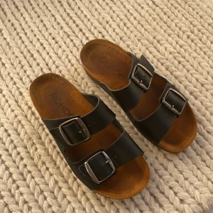 Svarta sandaler från Rohde - Snygga svarta sandaler från Rohde med två justerbara remmar och spännen. Perfekta för en avslappnad stil. Sandalerna har en bekväm fotbädd och en slitstark sula.