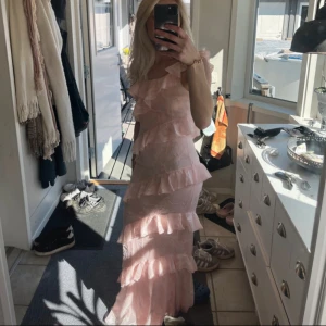 Ljusrosa lång volangklänning - Säljer en ljusrosa klänning med volanglager. Klänningen har en lång design och är perfekt för somriga tillfällen som bal. Den är oneshoulder och har en elegant passform. Jag säljer på grund av att den inte passade mig. 