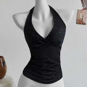 Svart glittrig halterneck topp - Snygg svart halterneck topp med glittrande detaljer. Toppen har en v-ringad design och knyts i nacken för en elegant look. Perfekt för en kväll ute eller festliga tillfällen.
