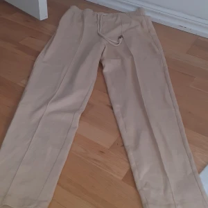 Beige mjukisbyxor med snörning - Säljer ett par bekväma beige mjukisbyxor med elastisk midja och snörning. Byxorna har en avslappnad passform och är perfekta för en chill dag hemma.
