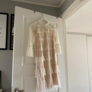 vit tyllklänning - Säljer en romantisk vit klänning från Vila med volanger och transparenta detaljer. Klänningen har trekvartsärmar och en hög hals med volangkant. Perfekt för en elegant look.