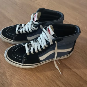 Svart och blå sneakers från Vans - Snygga svart och blå sneakers från Vans med vit sula och klassisk sidostrip. Skorna har snörning och en rund tå, perfekt för en avslappnad stil.