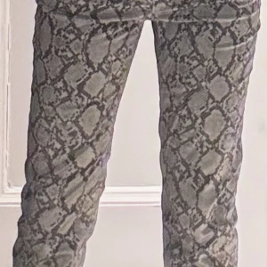 Ormmönstrade byxor - Snygga ormmönstrade byxor i grå och beige ton. Byxorna har en straight passform och är perfekta för att ge en trendig touch till din outfit. De är tillverkade i ett bekvämt material som passar bra för både vardag och fest.