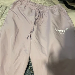 Ljuslila mjukisbyxor med tryck - Säljer ett par ljuslila mjukisbyxor med texten 'LIMITED EDITION' tryckt på sidan. Byxorna har en elastisk midja med dragsko för justerbar passform. Perfekta för en avslappnad stil.
